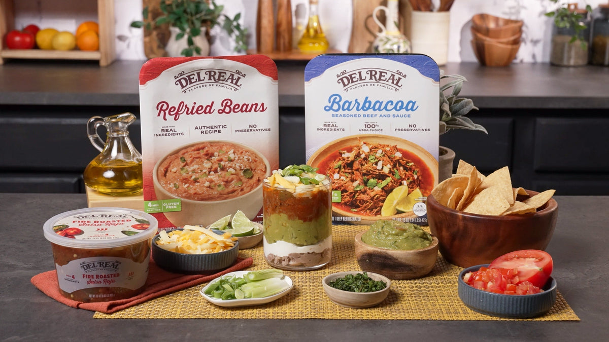 Layered barbacoa dip in a glass dish showing beans, sour cream, guacamole and cheese