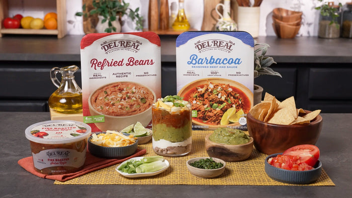 Layered barbacoa dip in a glass dish showing beans, sour cream, guacamole and cheese